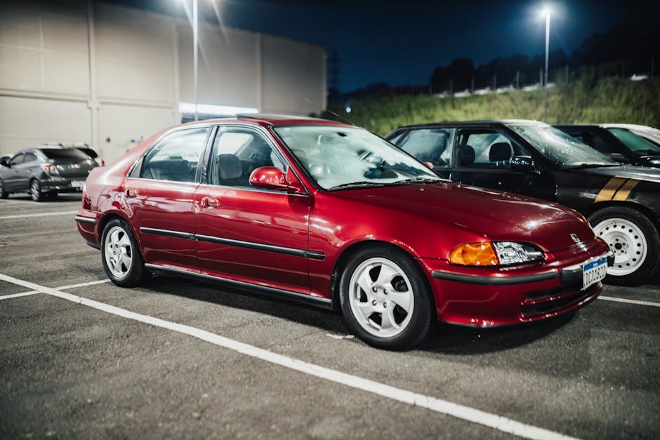A red Honda Civic parked under streetlights at a night car meet, showcasing retro automotive style.