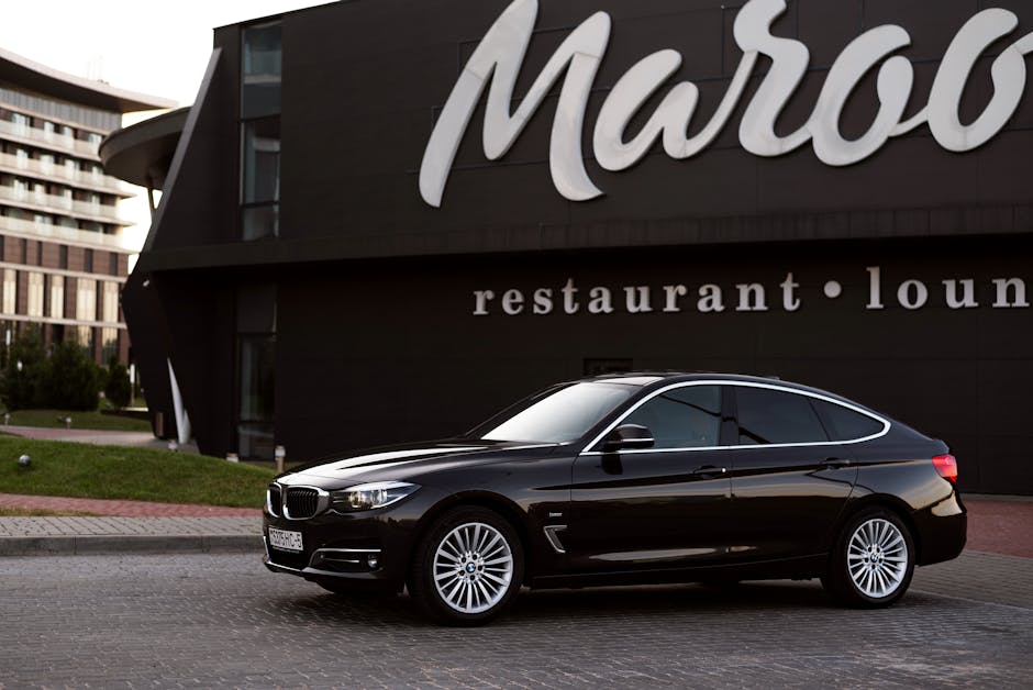 Black BMW sedan parked in front of stylish modern building with lounge signage, showcasing luxury and elegance.