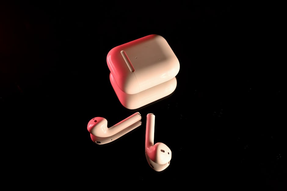 White wireless earbuds with a charging case, highlighted with red lighting on a reflective black surface.