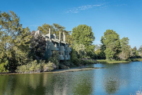 A contemporary riverside building nestled among lush green trees, reflecting in the water.