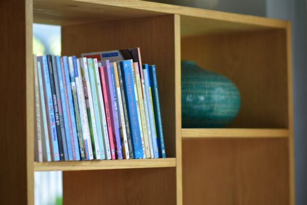 A collection of colorful children's books arranged on a wooden bookshelf with a decorative vase.