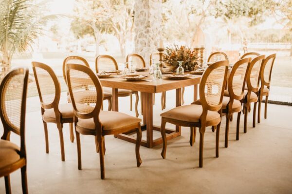 A beautifully arranged outdoor dining table with wooden chairs, glasses, and floral centerpiece.