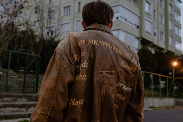 Back view of a man wearing a brown embroidered leather jacket standing in an urban setting.